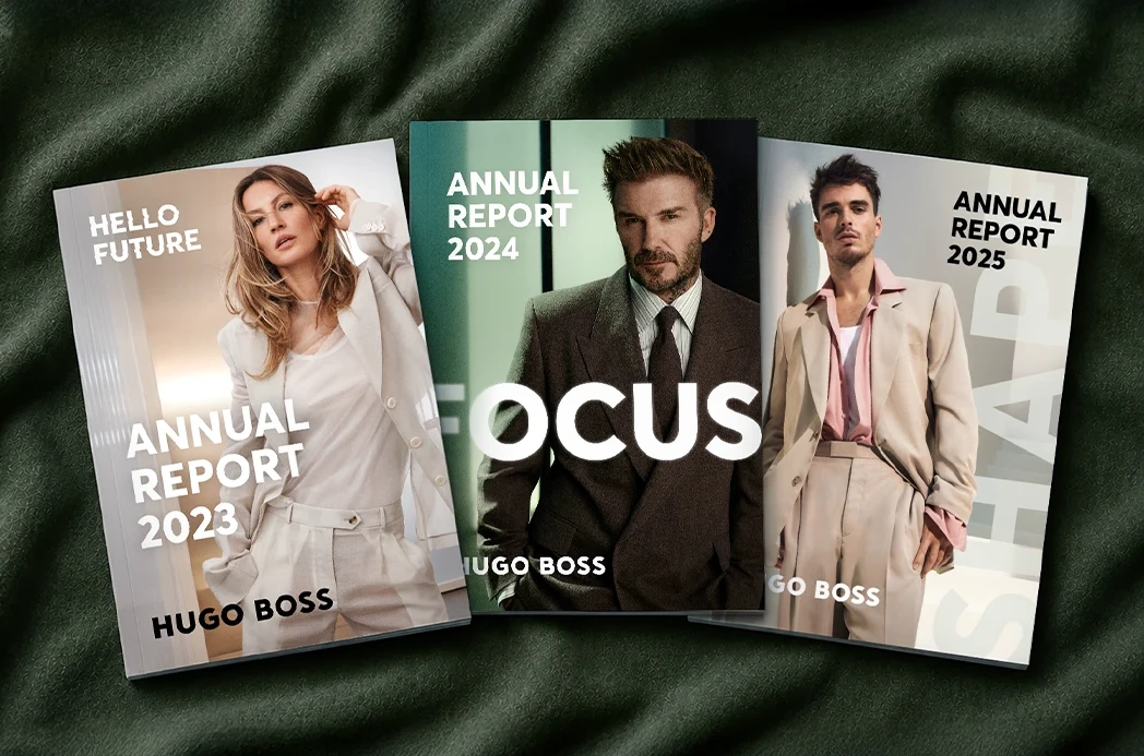 Three printed HUGO BOSS annual report covers fanned on dark green fabric — “Hello Future” 2023, “Focus” 2024 and “Shape” 2025, each with a fashion portrait